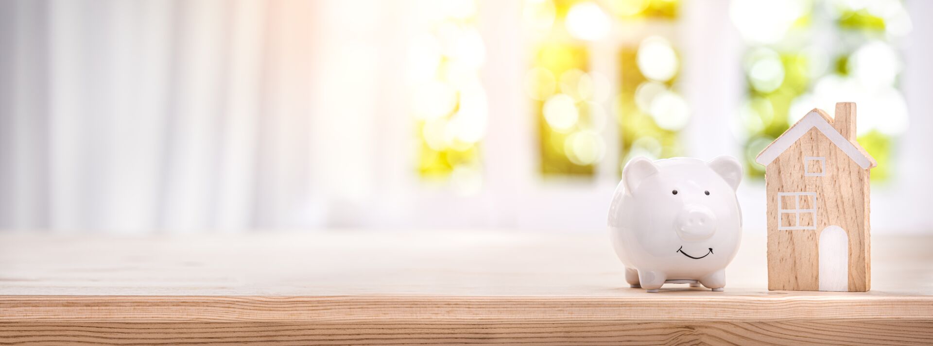 Sparschwein und kleines Holzhaus auf einem Tisch. Symbol für das Sparen für eine Immobilie mit Hauschulz Immobilien Service.