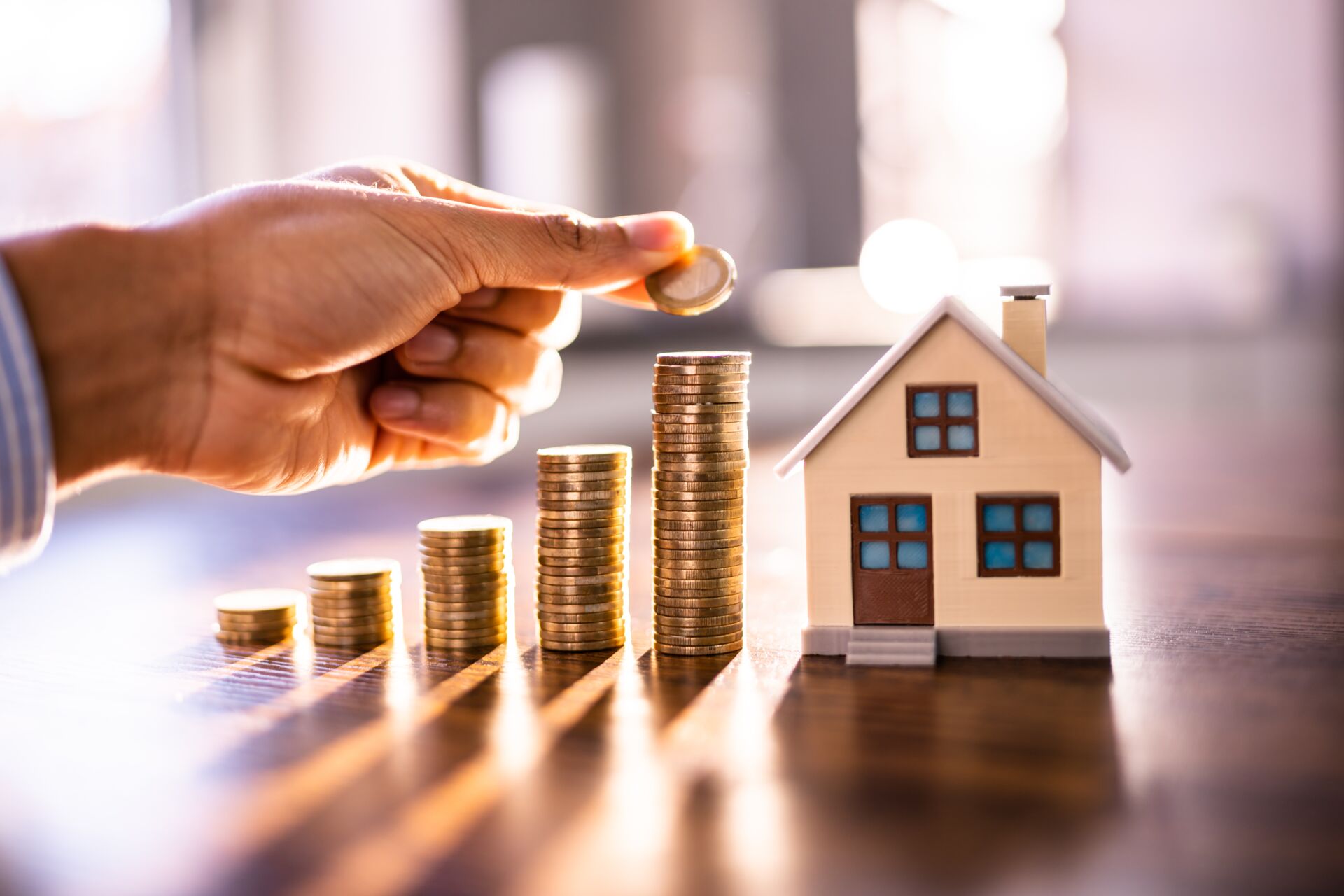 Hand legt Münze auf steigende Geldtürme neben einem Hausmodell. Symbol für Immobilieninvestition mit Hauschulz Immobilien Service.