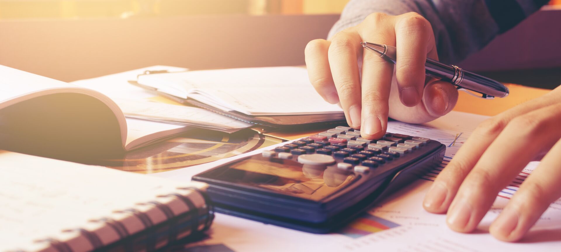 Hände tippen auf Taschenrechner über Finanzdokumenten. Symbol für Budgetplanung beim Immobilienkauf mit Hauschulz Immobilien Service.