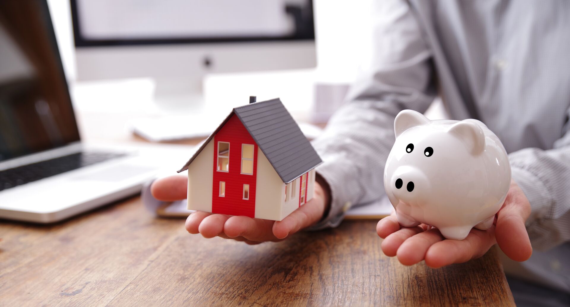 Hände halten ein Hausmodell und ein Sparschwein. Symbol für Immobilienfinanzierung und Sparen mit Hauschulz Immobilien Service.