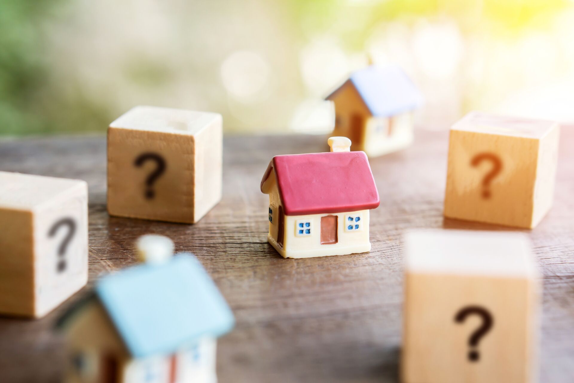Miniaturhäuser umgeben von Holzwürfeln mit Fragezeichen. Symbol für Fragen beim Immobilienverkauf mit Hauschulz Immobilien Service.